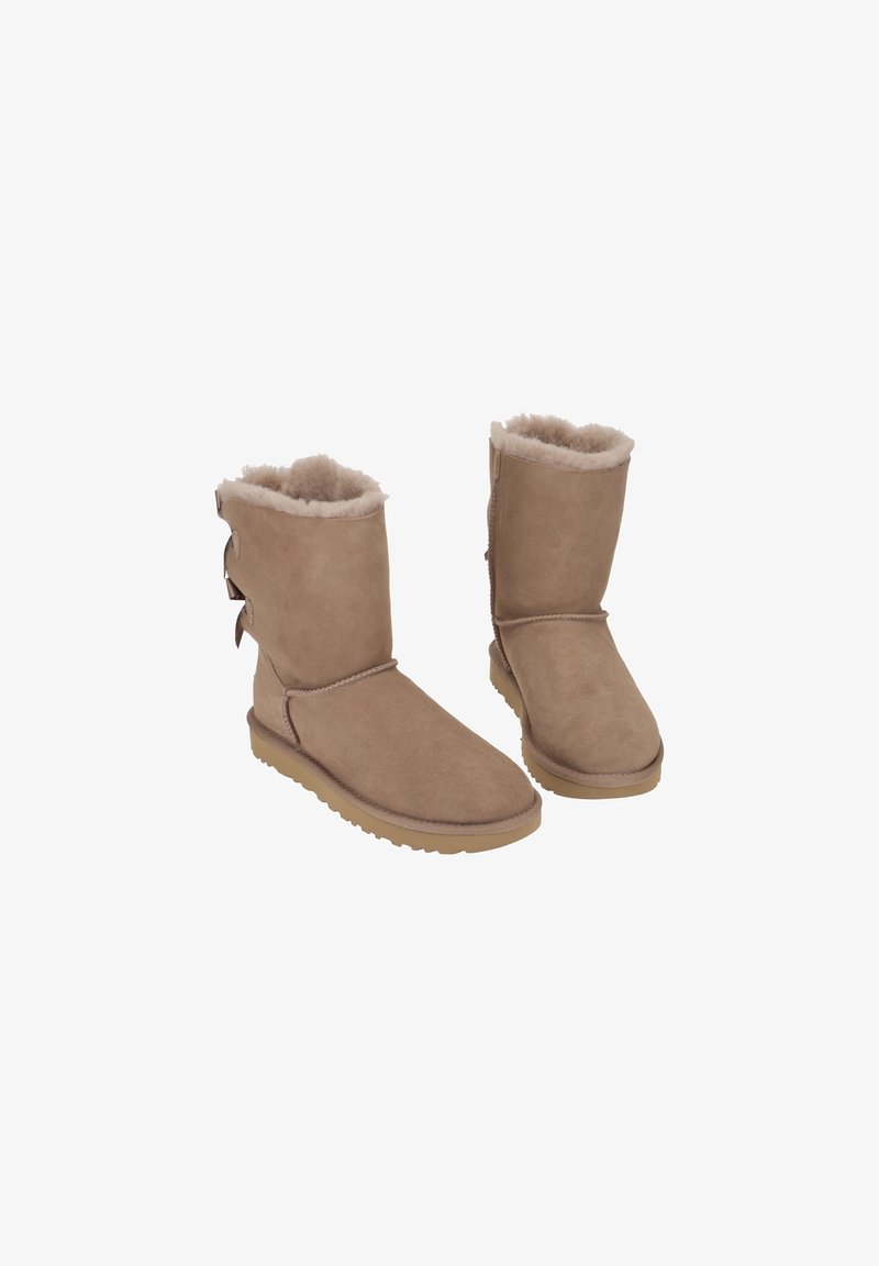 Bottes d'hiver mi-mollet couleur beige avec doublure en laine douce et trois nœuds décoratifs à l'arrière, semelles plates en caoutchouc, présentées sur fond blanc.
