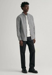 Black and white checkered button-up shirt with a collar, worn over a white t-shirt, paired with dark pants and black shoes.