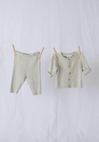 Ljusgrå ribbad stickad leggings och matchande kort cardigan med träknappar, hängande på en lina mot en vit bakgrund.