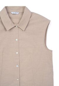 Camicia beige a maniche corte con colletto a punta, chiusura frontale con bottoni e tessuto texturizzato, caratterizzata da motivi sottili e senza tasche visibili.