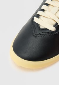 Must nahast toss, millel on sile pind, kreemika värvi paeladetail ja pehme kollane kummist tallaosa. Tekstuuriga õmblusdetailid.