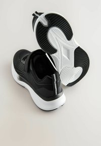 Baskets de sport noires avec un dessus tissé texturé, semelle intermédiaire blanche, semelle en caoutchouc et accents réfléchissants. Équipées d'une bande Velcro pour un maintien sécurisé.