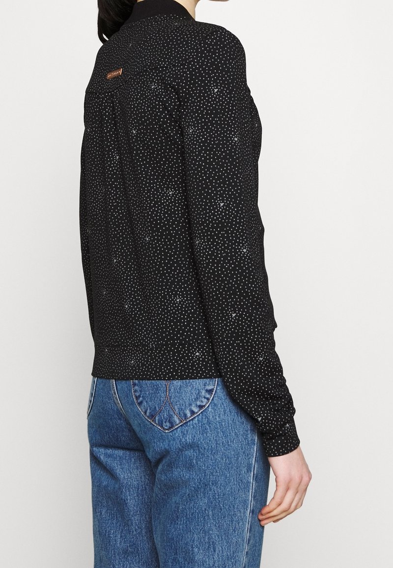 Svart långärmad topp med vita prickar, med krage och en rygghalsdetalj. Kombinerad med blå denimjeans.