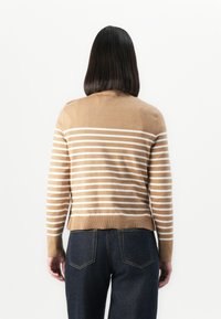Beige Pullover mit weißen horizontalen Streifen, gerippten Bündchen und Saum; getragen mit dunklen Jeans. Ansicht von hinten.