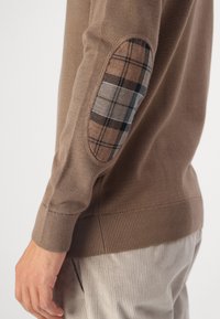 Pull en tricot marron avec des coudières à motifs tartan, des poignets et un ourlet côtelés. Texture douce avec une coupe ajustée.