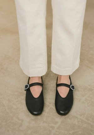 Scarpe nere di pelle con punta arrotondata, con cinturino in stile Mary Jane e una fibbia decorativa di colore argento, abbinate a jeans color crema.
