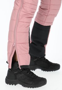 Gevoerde roze broek met zwarte accenten, voorzien van een zijrits en ribbelstructuur. Zwarte wandelschoenen met gestructureerde zolen.