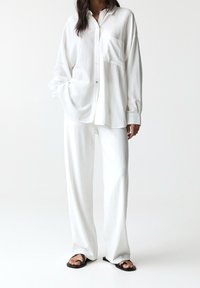 Camicia bianca larga con colletto e taschino sul petto, abbinata a pantaloni larghi coordinati. Tessuto liscio e morbido, design rilassato.