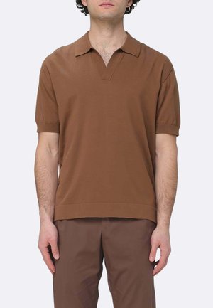 Uomo che indossa una polo marrone a maniche corte con collo a V e pantaloni marroni abbinati su uno sfondo uniforme.