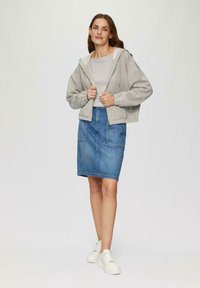 Grijze zip-up hoodie met witte voering, gecombineerd met een blauwe denimrok met voorzakken. Witte platform sneakers maken de look compleet.