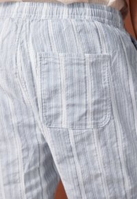 Lichtblauwe en witte gestreepte broek met een gestructureerde stof, voorzien van een elastische tailleband en een achterzak. Verticaal patroon ontwerp.