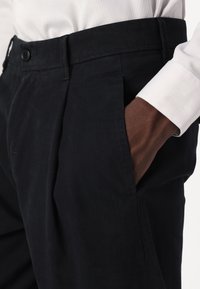 Marina byxor med rak gren, sidofickor och knappstängning vid midjan. Mönstrad tyg, skräddarsydd passform och slät yta.