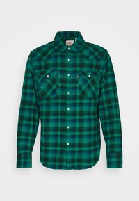 Camisa de cuadros verde y negra con cuello clásico, dos bolsillos frontales y botones de presión plateados, fabricada en un tejido suave.