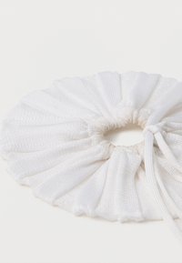 Λευκή υφασμάτινη σούρα με υφασμάτινη, μαζεμένη σχεδίαση και κυκλικό σχήμα. Διαθέτει ελαστική ταινία για ασφαλή εφαρμογή.