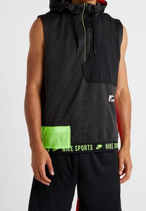 Sweat à capuche de sport noir sans manches Nike avec poche zippée vert néon, ourlet marqué, et short noir porté par une personne debout avec les bras détendus.