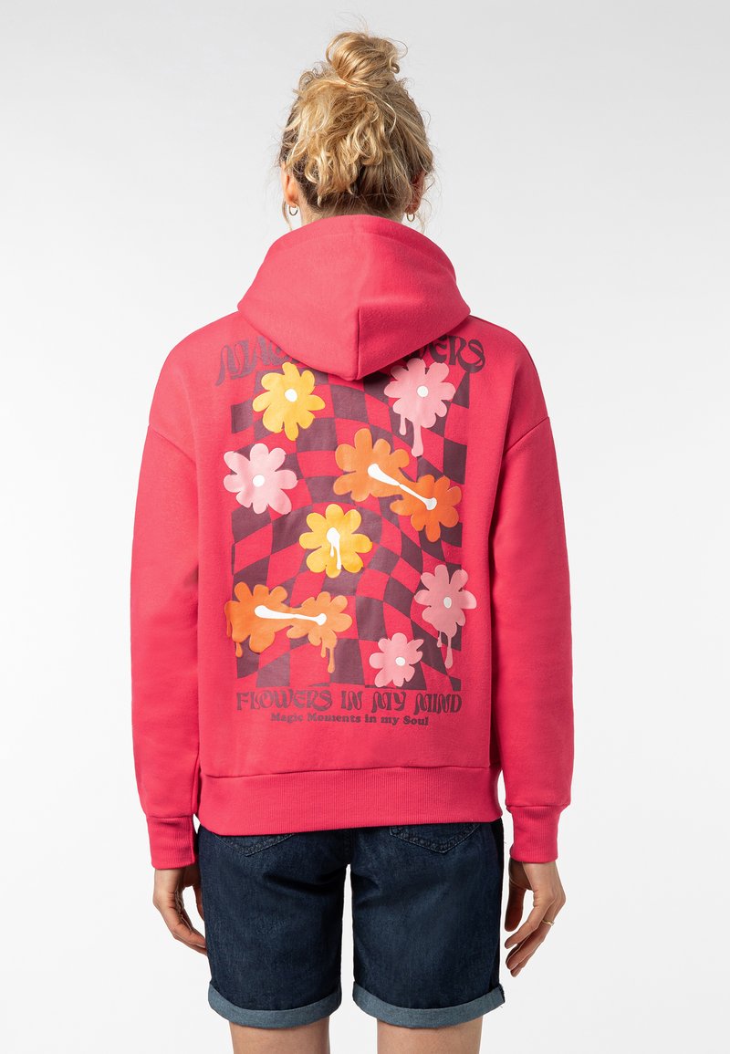 Roze hoodie met een geblokt bloemmotief in levendige kleuren aan de achterkant. Heeft een capuchon en geribbelde manchetten. Casual fit, gecombineerd met donkere shorts.