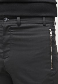 Schwarze Hose aus glattem Stoff, mit einem Reißverschlussfach, einem Knopfverschluss und schmaler Passform. Strukturierte Oberfläche mit minimaler Gestaltung.