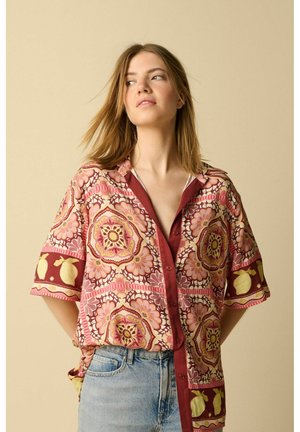Jeune femme portant une chemise à manches courtes à motifs floraux et citrons, associée à un jean bleu clair, regardant sur le côté.
