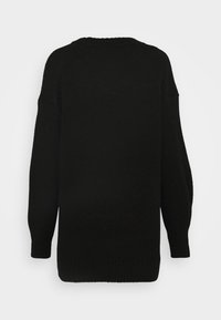 Pull noir en maille oversize avec manches longues et poignets et ourlet côtelés, vu de dos sur un fond clair uni.