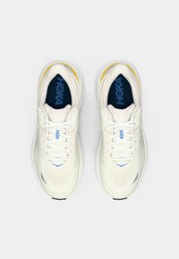 Um par de sapatilhas de corrida HOKA brancas com detalhes em azul e amarelo, vistas de cima sobre um fundo branco puro.