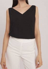 Top negro sin mangas con un diseño de escote en V, hecho de una tela suave. Presenta un corte relajado y cae justo por debajo de la cintura.