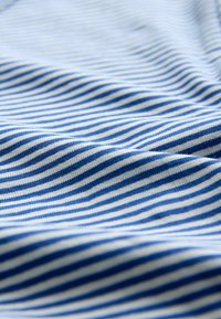 Bomuldsstof med skiftende blå og hvide striber, der udviser en blød tekstur og en let krøllet overflade.