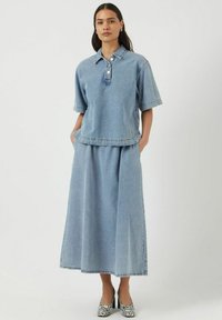 Outfit in denim con una maglietta colletto a maniche corte e una gonna lunga abbinata. Colore azzurro chiaro con orlo strappato e due tasche laterali.
