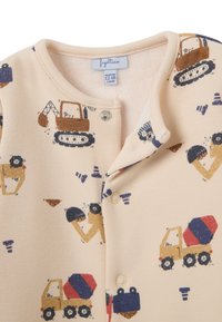Monos infantil beige con vehículos de construcción y herramientas impresas, que cuenta con cierres a presión y un suave forro de polar.