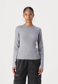 Pull gris à manches longues en rib avec col rond, silhouette ajustée et texture douce, associé à un pantalon noir en peluche avec poches.