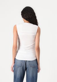 White sleeveless top with ruched texture, soft fabric, and a fitted design. Paired with light blue high-waisted jeans.