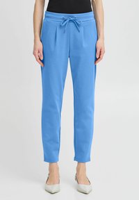 Light blue sweatpants with a drawstring waist, pleated front design, tapered legs, and soft fabric texture.