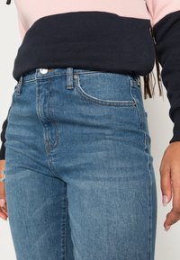 Jeans de cintura alta azul-escuro feitos de denim com um leve desgaste, costura discreta e ligeira desgastação na área dos bolsos traseiros.