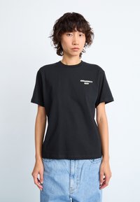 Black cotton t-shirt with short sleeves, crew neck, and small white graphic text on the chest. Paired with light blue denim.