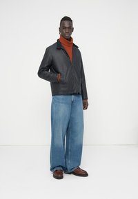 Μαύρο δερμάτινο μπουφάν με γιακά, φερμουάρ μπροστά και πλαϊνές τσέπες. Φορεμένο πάνω από ένα ψηλό λαιμό σε σκουροκόκκινο χρώμα, συνδυασμένο με φαρδιά μπλε τζιν και καφέ παπούτσια.