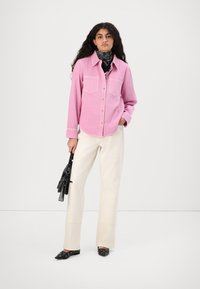 Pink button-up shirt with two chest pockets, cream wide-leg trousers, and black embellished shoes. Black scarf around the neck.