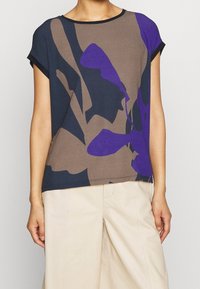 Krátký rukáv top v námořnické modré, hnědé a fialové barvě s výrazným abstraktním vzorem. Měkká tkanina a volný střih, s kulatým výstřihem.