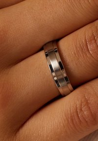 Zilveren metalen ring met een gladde, gepolijste oppervlakte en twee duidelijke banden. Draagt om een vinger met zichtbare huidtextuur en rimpels.
