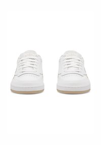 Fehér sportcipők sima bőrből készült felső résszel, fehér fűzőkkel és bézs gumitalppal. A lábujj betét perforált részletekkel rendelkezik.