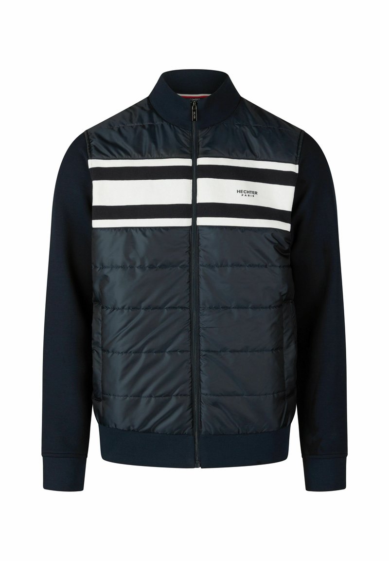 Marineblauwe jas met een gewatteerde bovenkant, witte en zwarte horizontale strepen, ritssluiting aan de voorkant en ribgebreide manchetten. Gemaakt van gemengde materialen voor warmte.