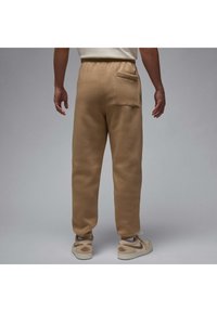 Khaki sweatpants made of soft fabric, featuring a back pocket and a relaxed fit, paired with light-colored sneakers.