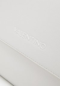 Vit läderväska med strukturerad yta, med präglad "Valentino"-logotyp och ren sömnad längs kanterna.