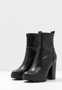 Botas de cuero negras hasta el tobillo con un diseño elegante, que cuentan con un tacón alto grueso, lengüetas para facilitar el calce y suela de goma para mayor tracción.