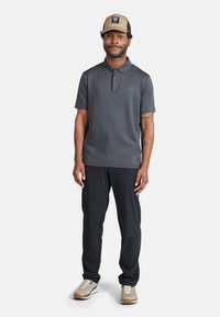 Polo shirt gris foncé avec un col, associé à un pantalon noir. Porte une casquette marron clair et noire avec un logo. Chaussures de sport beiges.