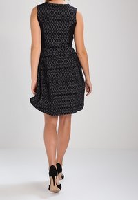 Svart och mönstrad ärmlös klänning med figurnära overdel och utsvängd kjol, kombinerad med svarta högklackade skor.