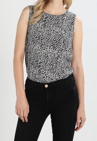 Svart och vit ärmlös topp med en strukturerad abstrakt mönster, tillverkad av lättviktig tyg, kombinerad med högmidjade svarta jeans.