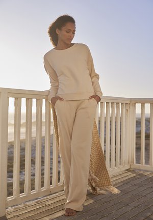 Beige ribbed sweater and matching wide-leg pants, featuring a relaxed fit, soft texture, and a side slit accent, against a natural backdrop.