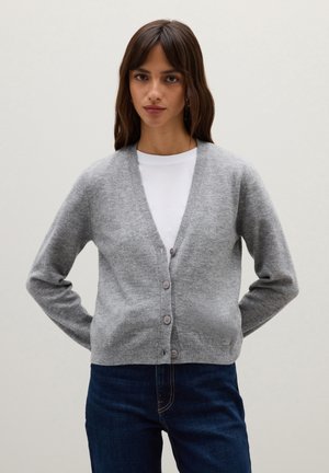 Grauer Cardigan aus weichem Strickstoff, mit V-Ausschnitt, langen Ärmeln und einer Knopfleiste mit fünf Knöpfen. Über einem weißen Hemd mit blauen Jeans getragen.