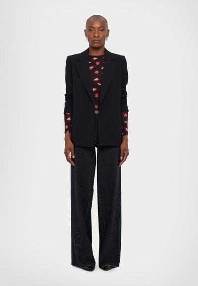 Black blazer layered over a red lip-patterned top, paired with sparkling black wide-leg pants. Smooth fabric with shiny accents.