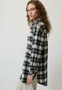 Karirana košulja s crnom, bijelom i sivom bojom, dugim rukavima, ovratnikom i opuštenim krojem, s malo produženim stražnjim rubom.