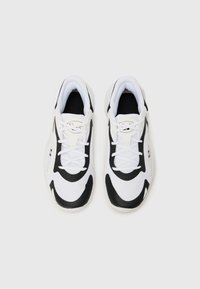 White and black athletic shoes featuring a mesh upper, curved design, textured accents, and flat laces. Distinct logo on the tongue.